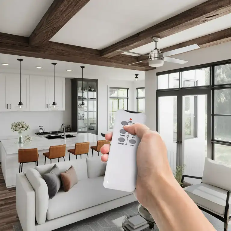 Hand holding a remote control in a modern living room with wooden beam ceilings, a kitchen island, and large windows.