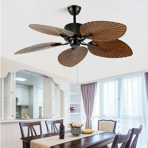 Ceiling fan with leaf-shaped blades above a dining table set with a wine bottle and glasses in a bright room with large windows.