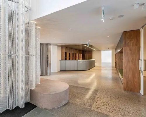 Modern reception area with minimalist design, featuring a curved desk, wooden panels, and perforated metal partitions.